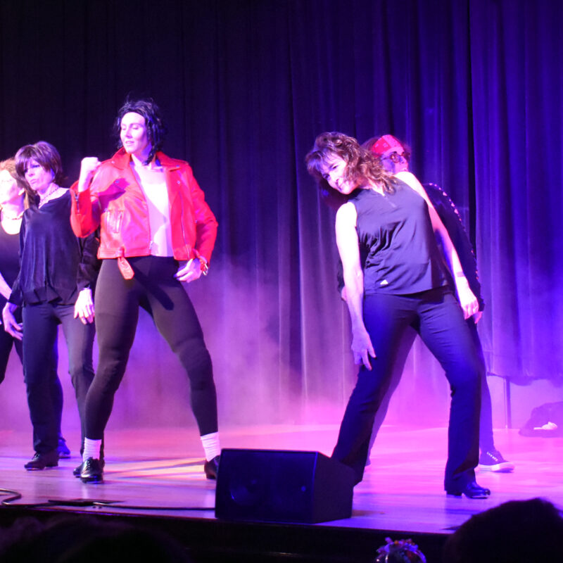 group of people dancing on a purple stage that has fog