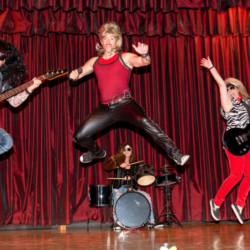 four performers dressed as a rock band jumping up on the stage