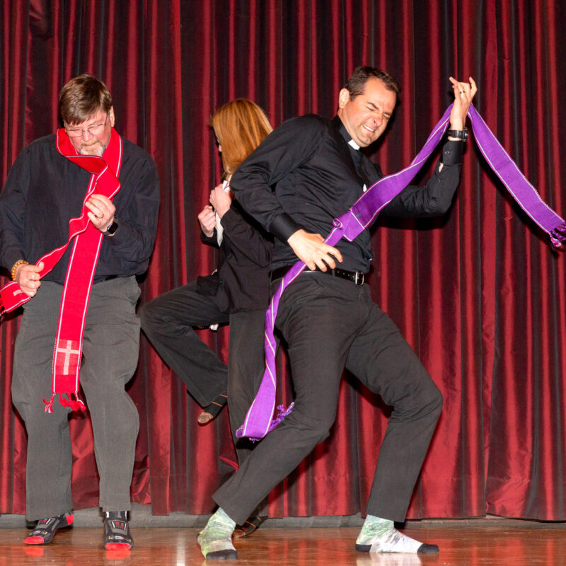 three performers dressed as catholic priests