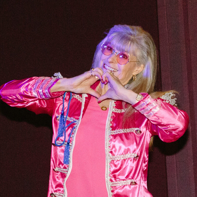 woman in a pink outfit and pink sunglasses making a heart symbol with her hands