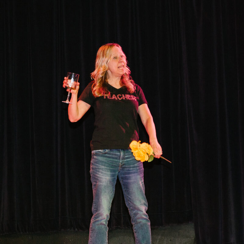 woman on a stage holding up a glass and flowers