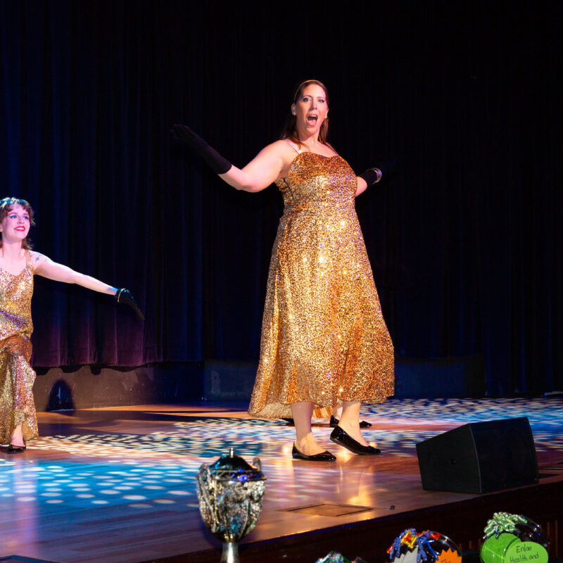 two women on a stage wearing gold dresses