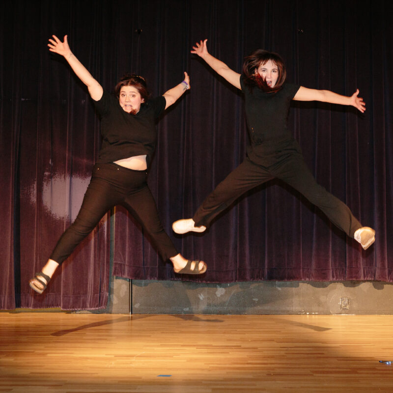 two women on a stage jumping up with their hands up